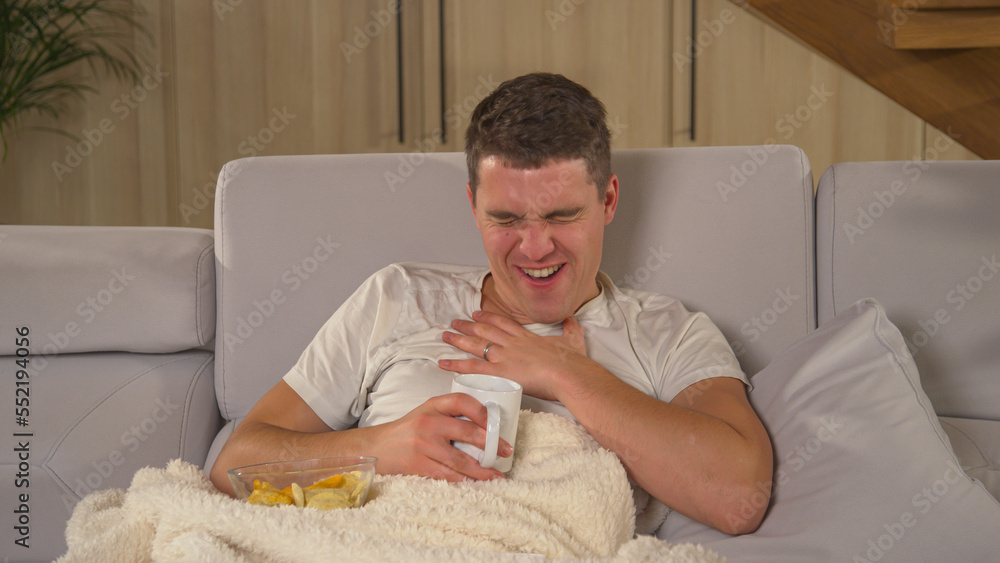 CLOSE UP: Laughing man watching funny comedy movie and drinking tea