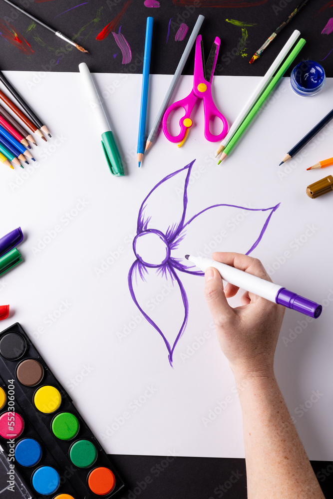 Vertical image of hand drawing purple flower on paper and art materials on table top, copy space