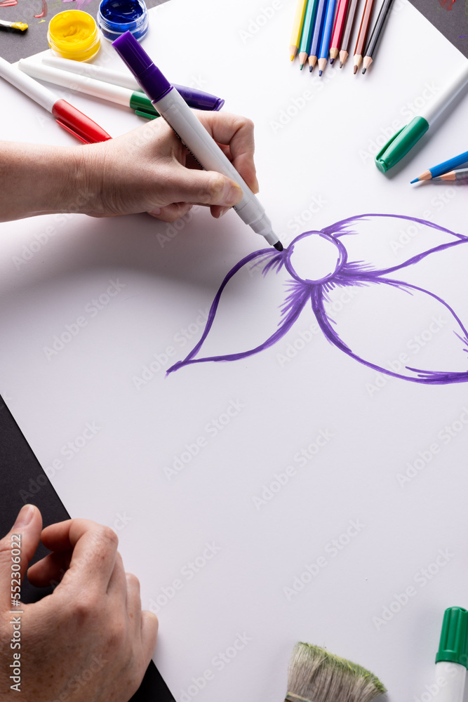 手在纸上画紫色花朵的垂直图像，桌面上的艺术材料，复制空间