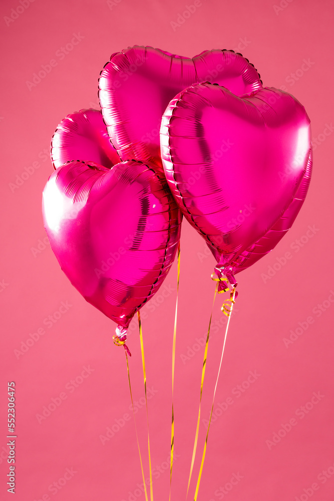 四个闪亮的粉红色心形气球垂直漂浮在白色背景上，带有复制空间