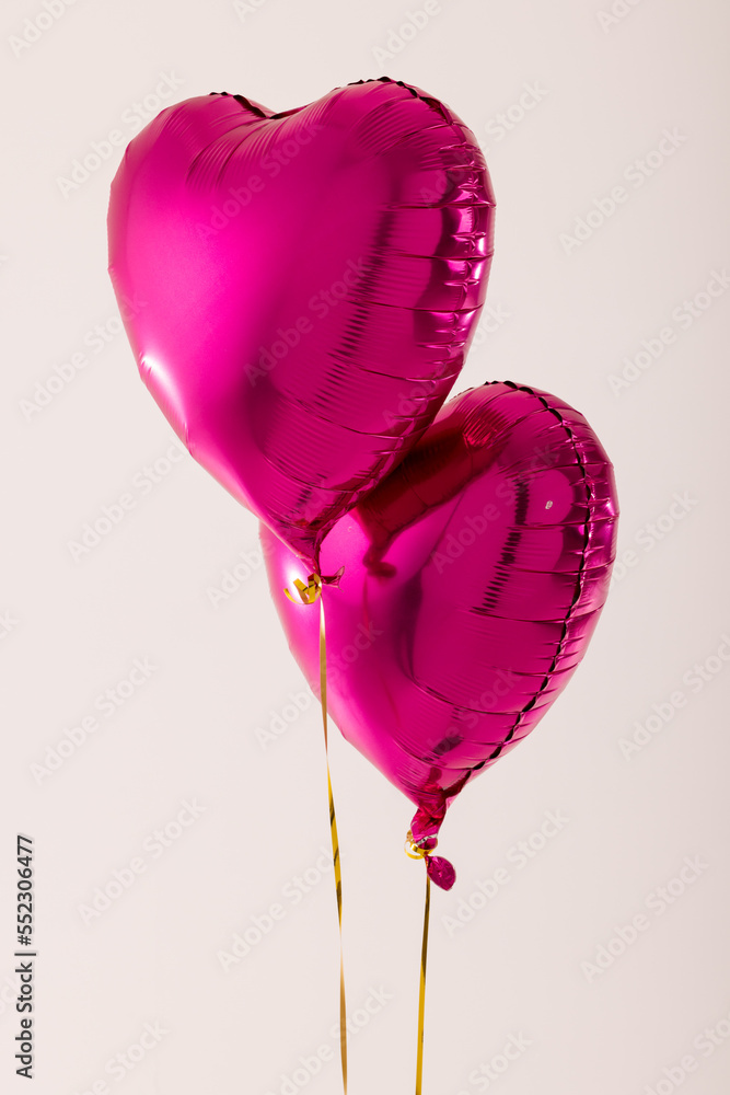 两个闪亮的粉红色心形气球垂直漂浮在白色背景上，带有复制空间