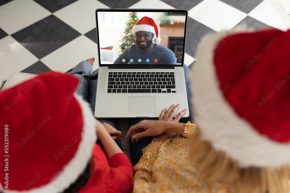 戴着圣诞老人帽的高加索母女在圣诞笔记本电脑上与非裔美国人视频通话