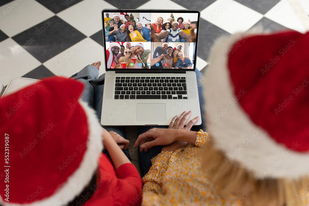 Caucasian mother and daughter in santa hats having christmas laptop video call with diverse friends