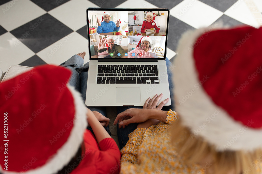 Caucasian mother and daughter in santa hats on christmas laptop video call with diverse friends