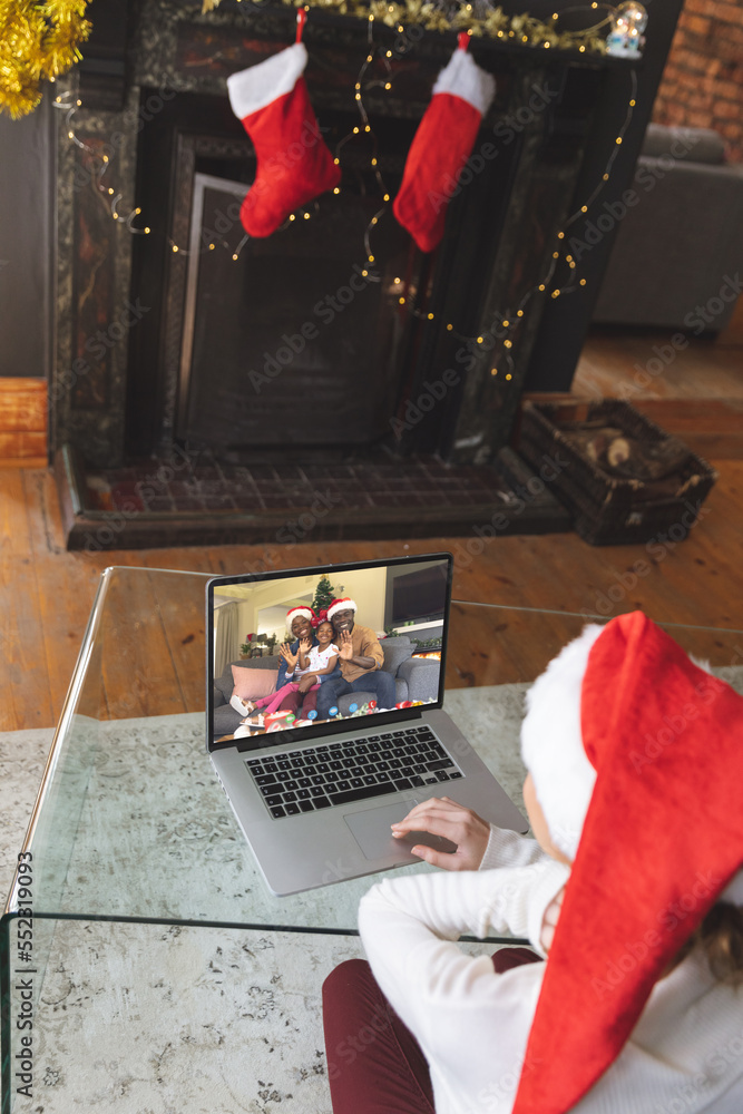 戴着圣诞老人帽的白人妇女与幸福的非裔美国人家庭进行圣诞笔记本电脑视频通话