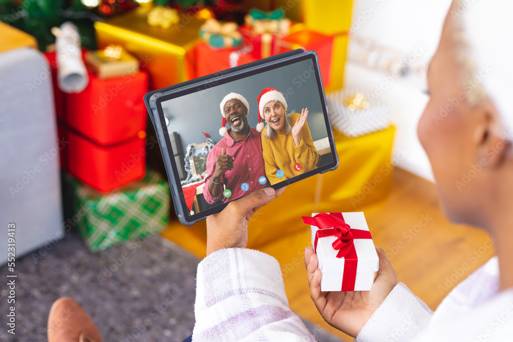 African american woman with christmas decorations having video call with happy diverse couple