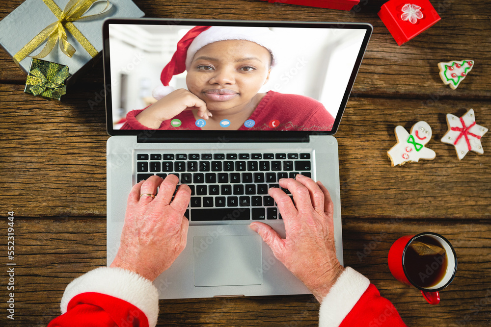 Santa claus with christmas presents having video call with happy african american woman