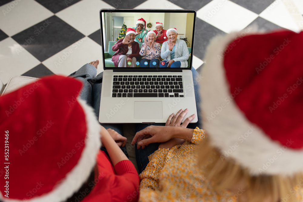 Diverse mother and daughter with santa hats having video call with happy senior diverse friends