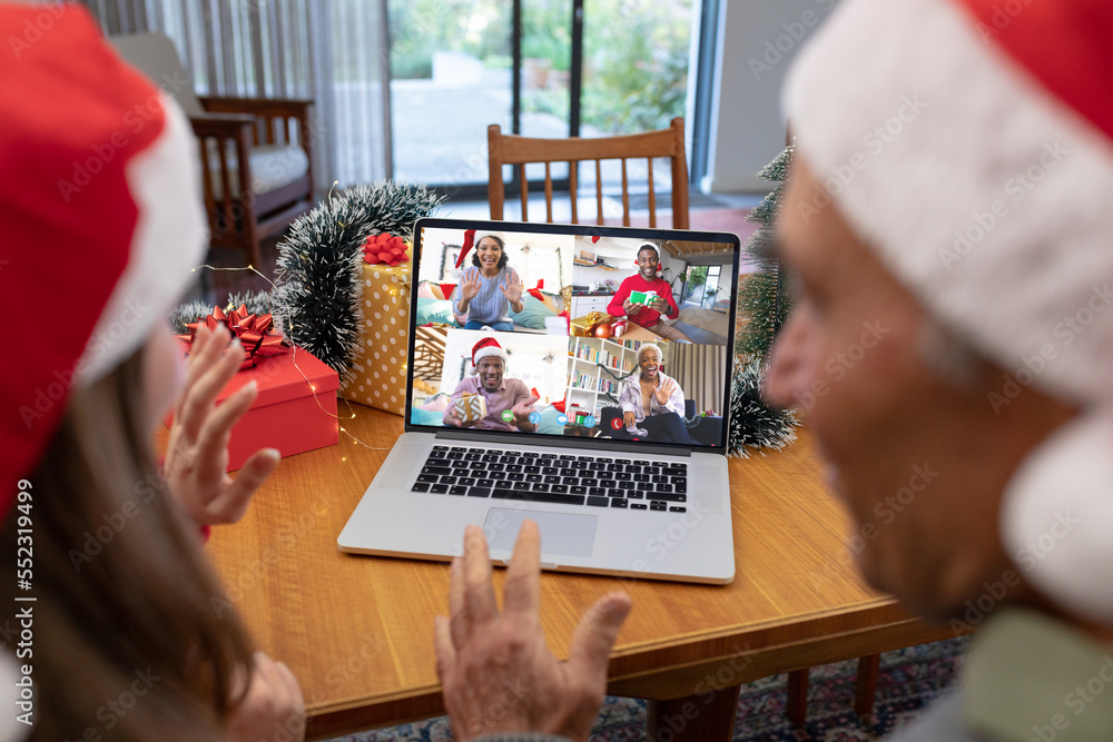 Caucasian father and daughter with santa hats having video call with happy diverse friends