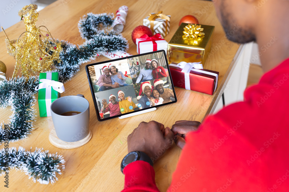 African american man with christmas presents having video call with happy diverse friends