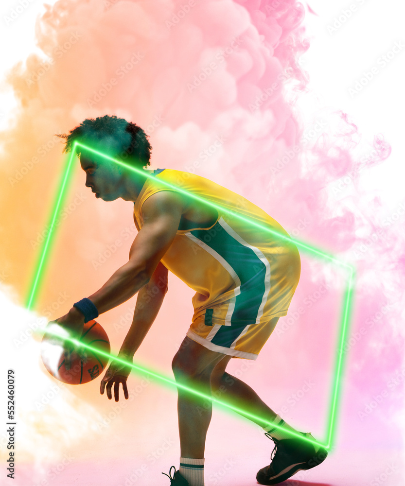 Side view of biracial male player dribbling basketball by rectangle over smoky background