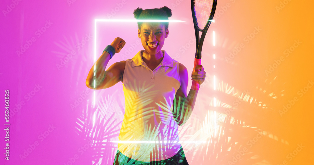 Cheerful biracial tennis female player with racket clenching teeth by illuminated square and plants