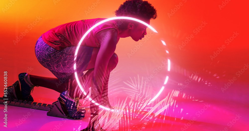 Side view of biracial female athlete at starting position by illuminated circle and plants