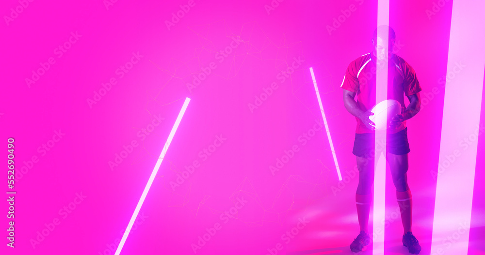 Full length of african american rugby player holding ball over illuminated lines on pink background