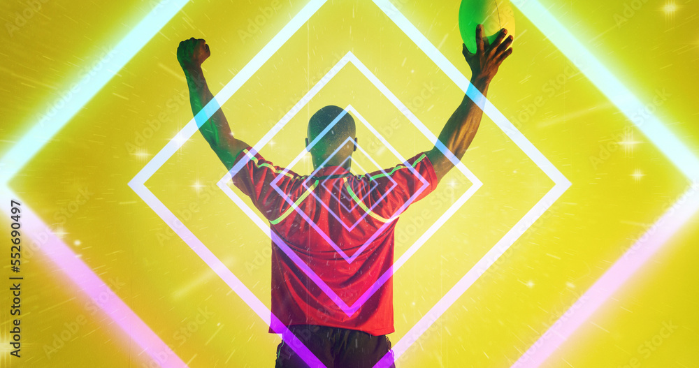 Illuminated square shapes over rear view of african american rugby player raising arms with ball