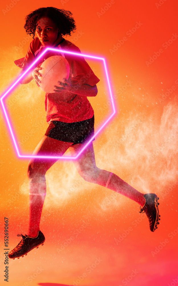Biracial female rugby player with ball jumping over illuminated hexagon and abstract pattern