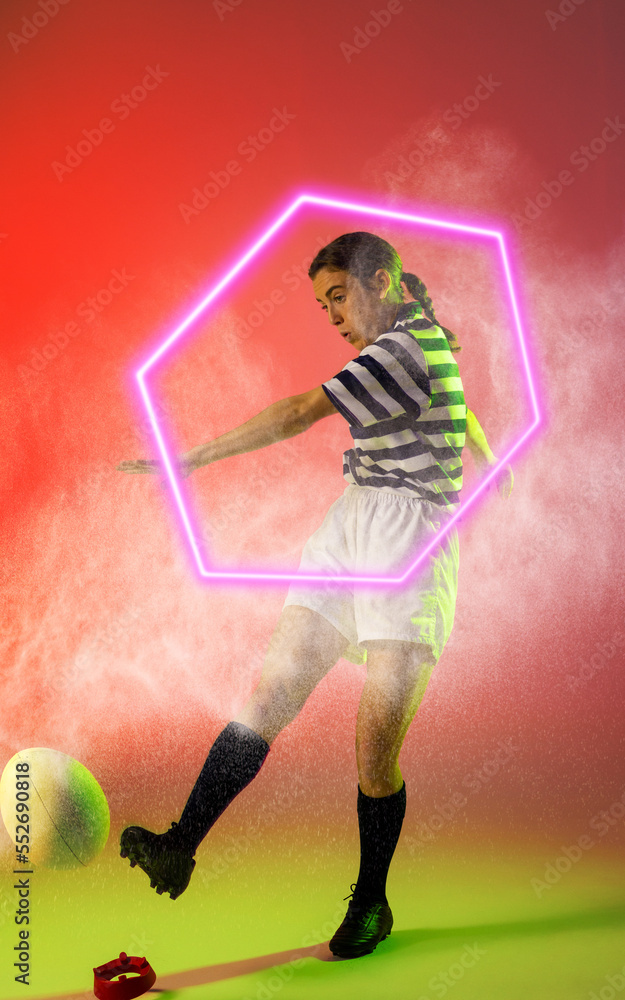 Illuminated hexagon over caucasian female rugby player kicking ball amidst smoke, copy space
