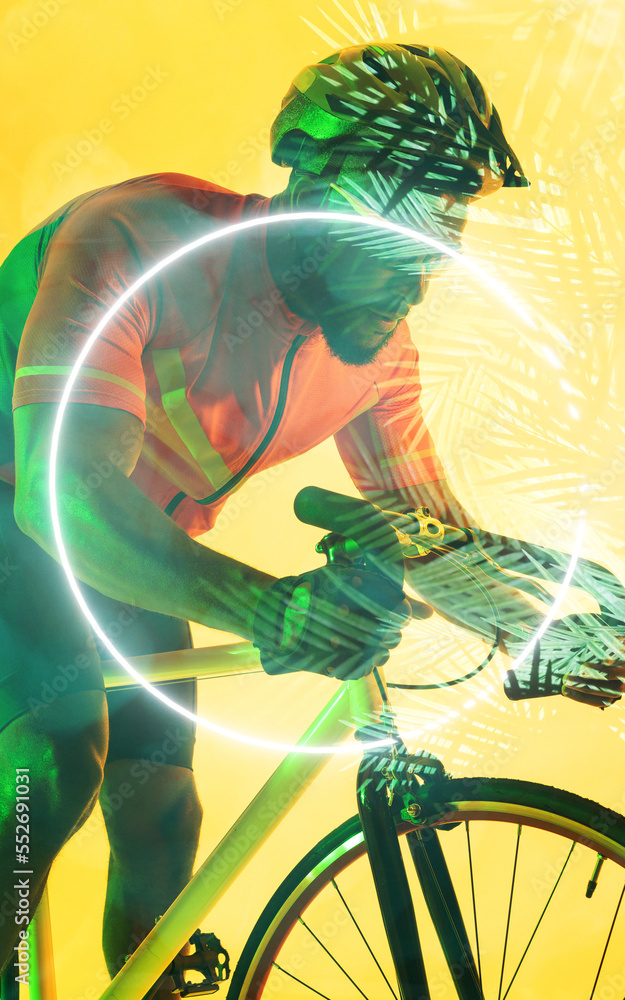 African american male cyclist riding bike by glowing circle and plants over yellow background