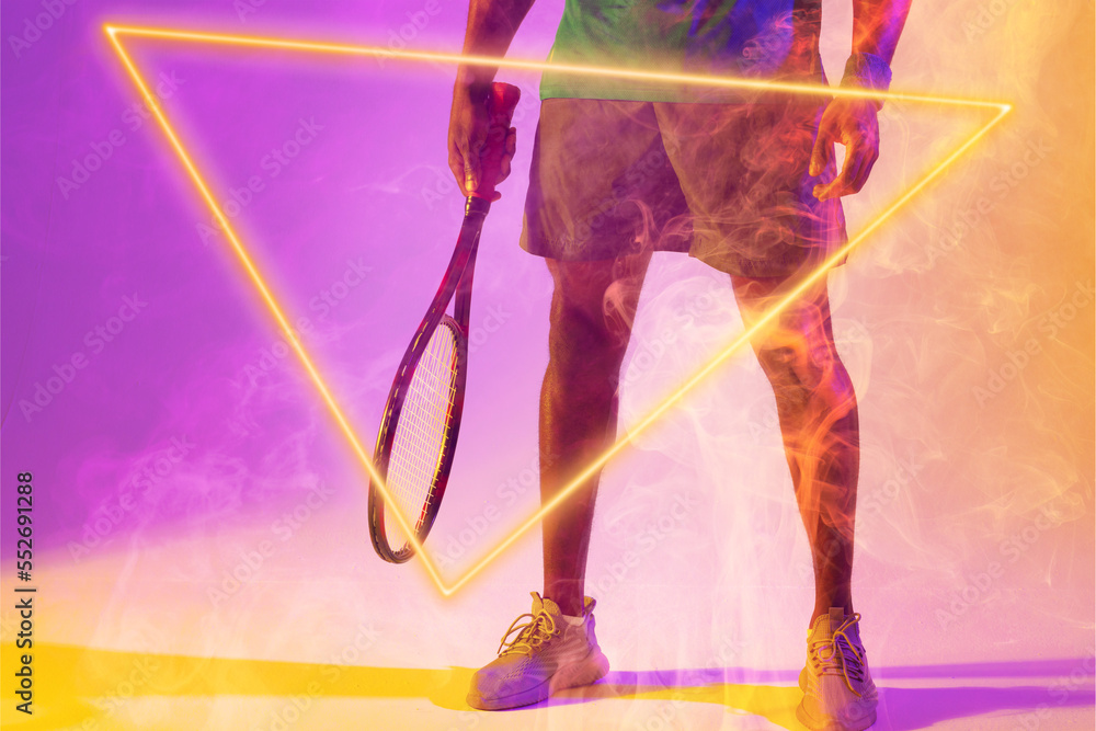 Low section of african american male tennis player with racket amidst smoke by illuminated triangle