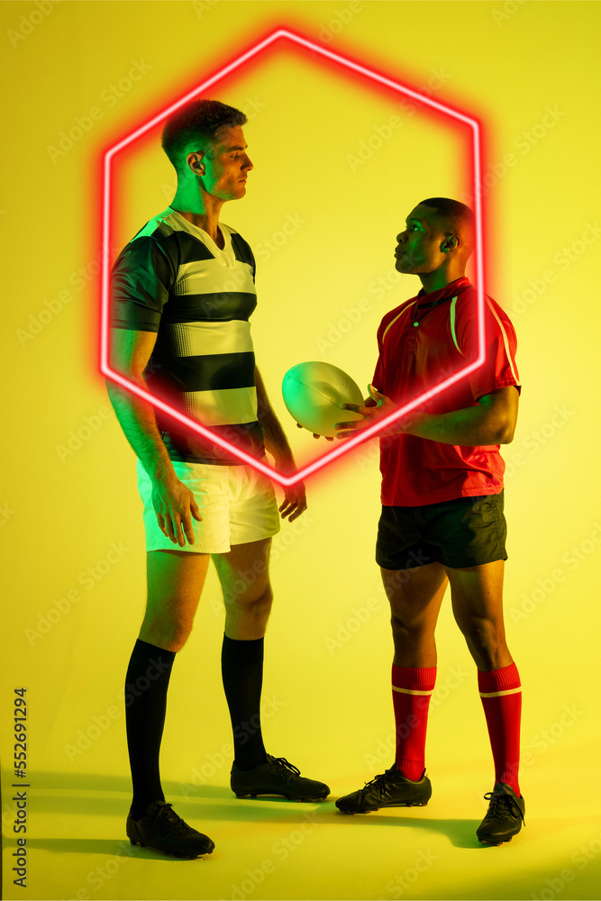 Multiracial male rugby opponents staring at each other by glowing hexagon over yellow background