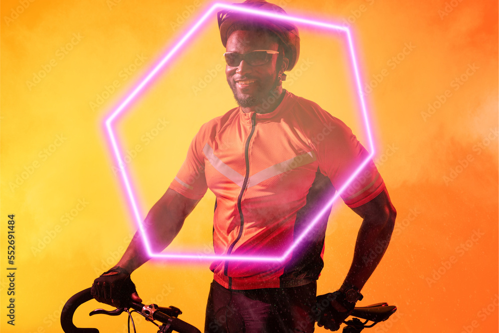 Smiling african american male athlete wearing helmet and glasses with bike by illuminated hexagon