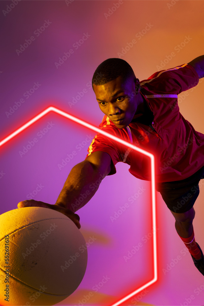 African american male rugby player catching ball by illuminated hexagon on gradient background