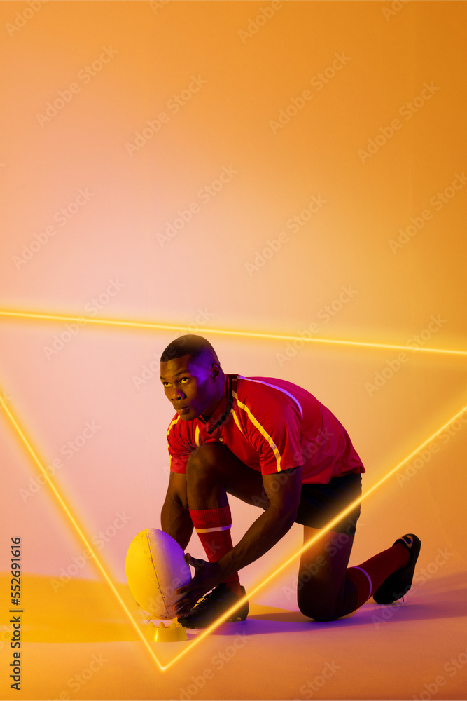 自信的非裔美国男子橄榄球运动员将球放在照亮的三角形看台上