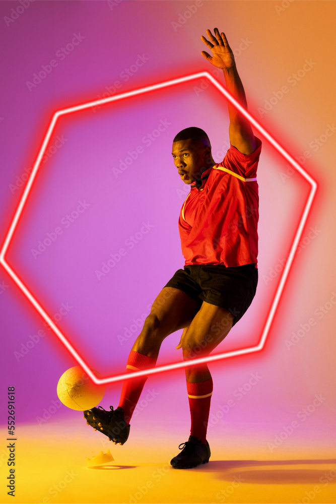 African american male rugby player kicking ball by illuminated hexagon over gradient background
