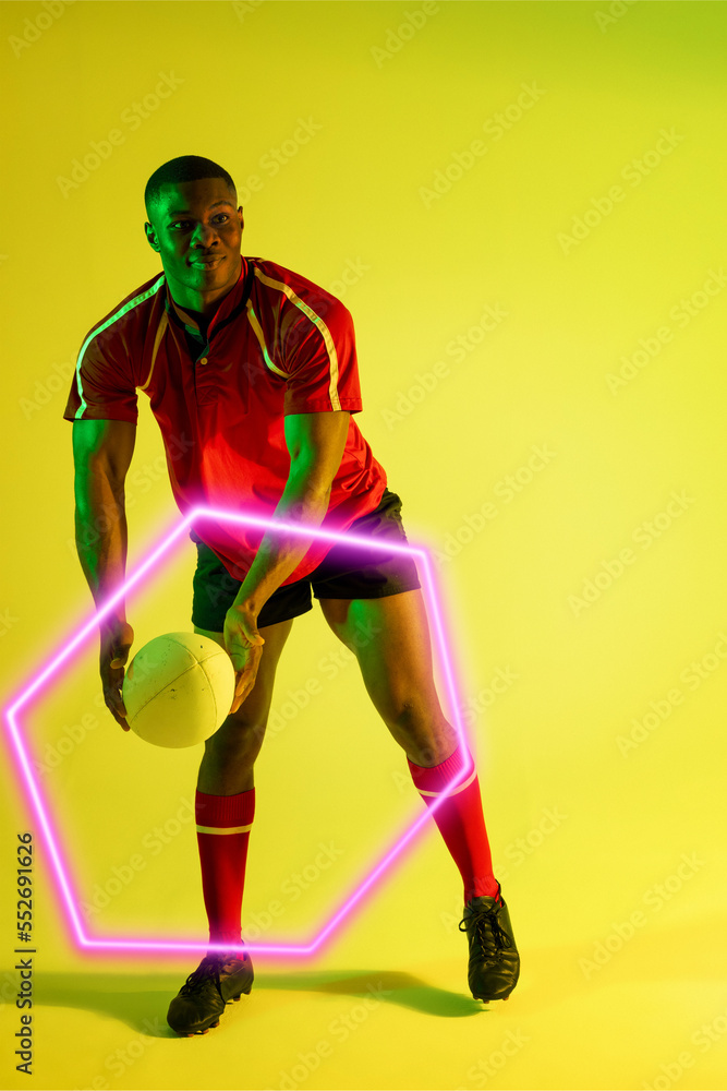 Smiling african american male player throwing rugby ball by illuminated hexagon on green background
