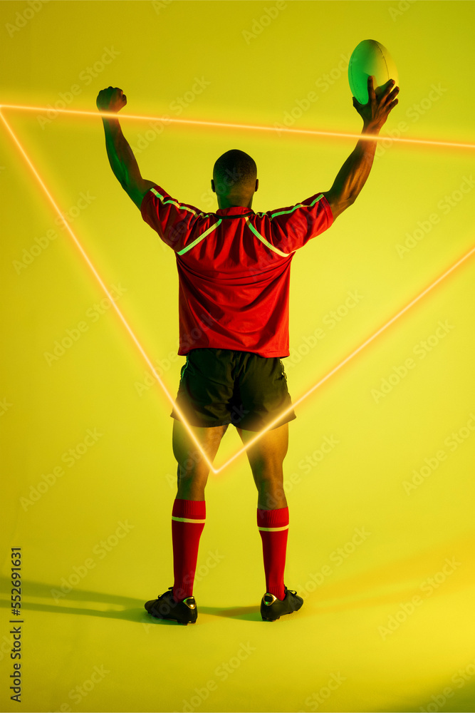 Illuminated triangle over rear view of african american male rugby player with ball raising arms