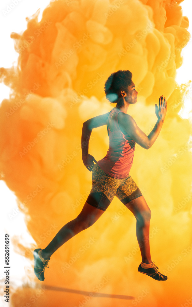 Side view of african american female athlete with afro hair running over orange smoky background