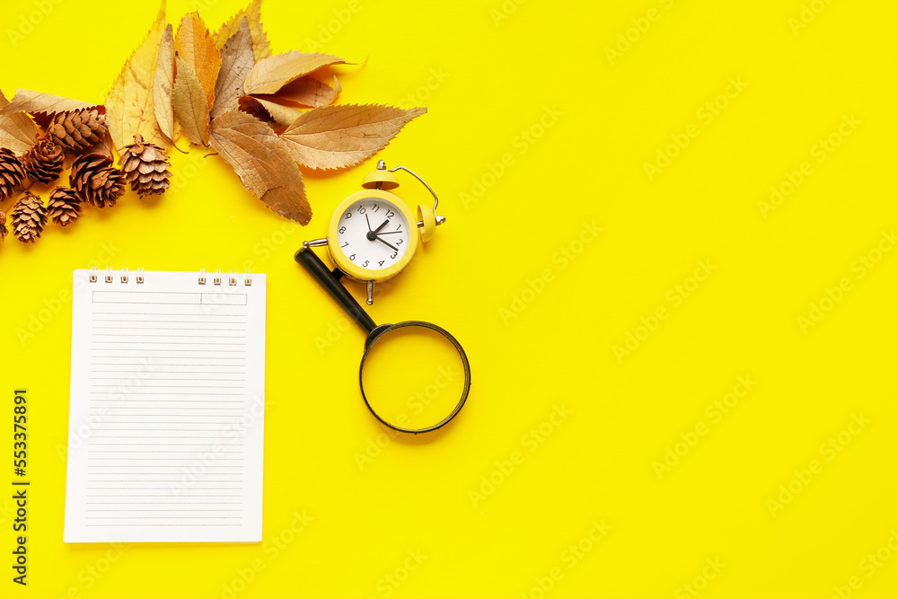 黄色背景上有笔记本、秋叶、圆锥体、闹钟和放大镜的构图