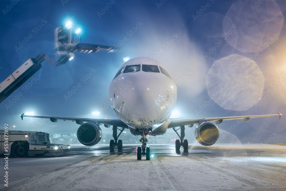 Deicing of airplane before flight. Winter night at airport during snowfall..