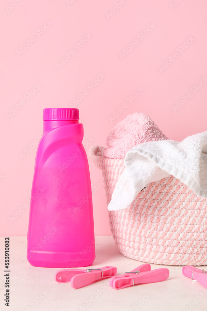 粉红色背景下桌子上的洗衣粉、衣夹和篮子