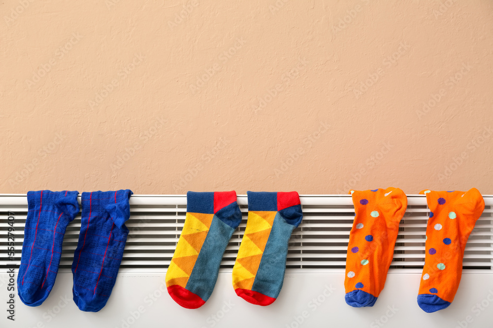 Warm socks drying on electric radiator near beige wall, closeup