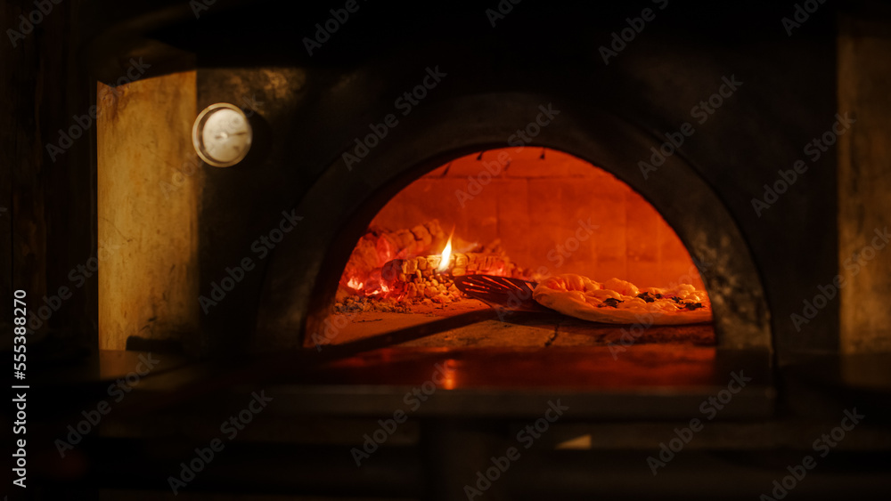 餐厅内专业厨师在木火石炉中使用披萨皮制作披萨。传统