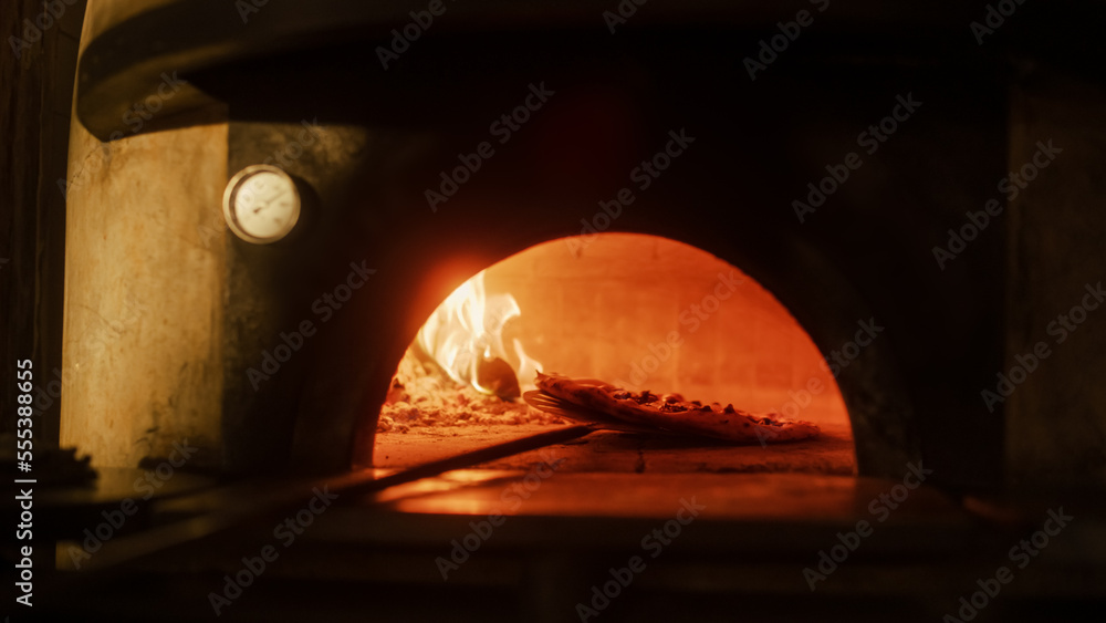 餐厅内披萨皮将披萨转移到木火石炉中。传统烹饪，意大利