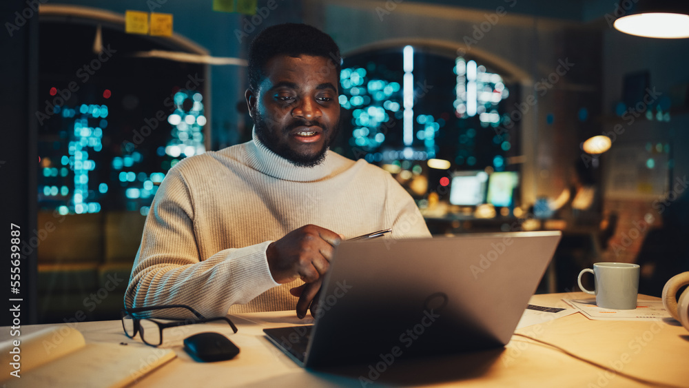 一位英俊的黑人项目经理在一个晚上用笔记本电脑进行视频通话的肖像
