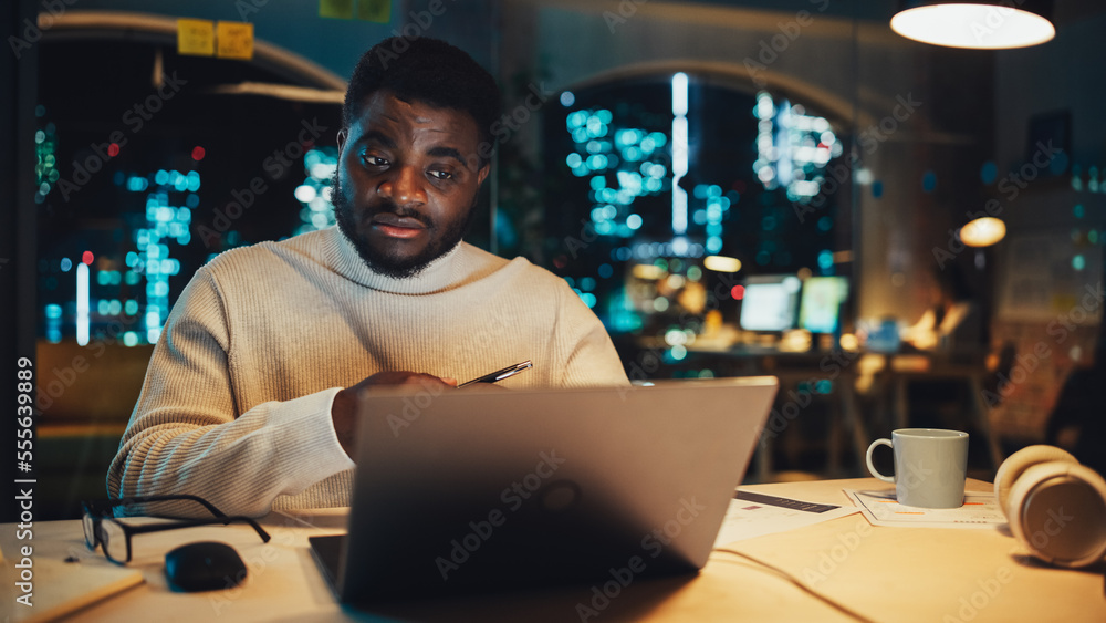 英俊的黑人项目经理在晚间办公室环境中用笔记本电脑进行视频通话