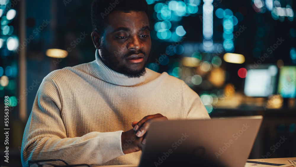 英俊的黑人项目经理在夜间办公室环境中用笔记本电脑进行视频通话