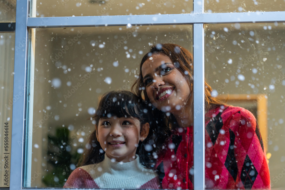 可爱的孩子看着窗户，和妈妈一起欣赏雪花。