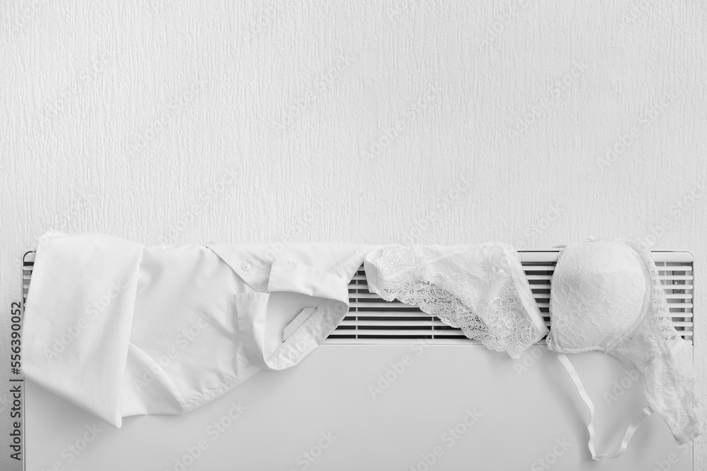 Female underwear and shirt drying on electric radiator near light wall, closeup