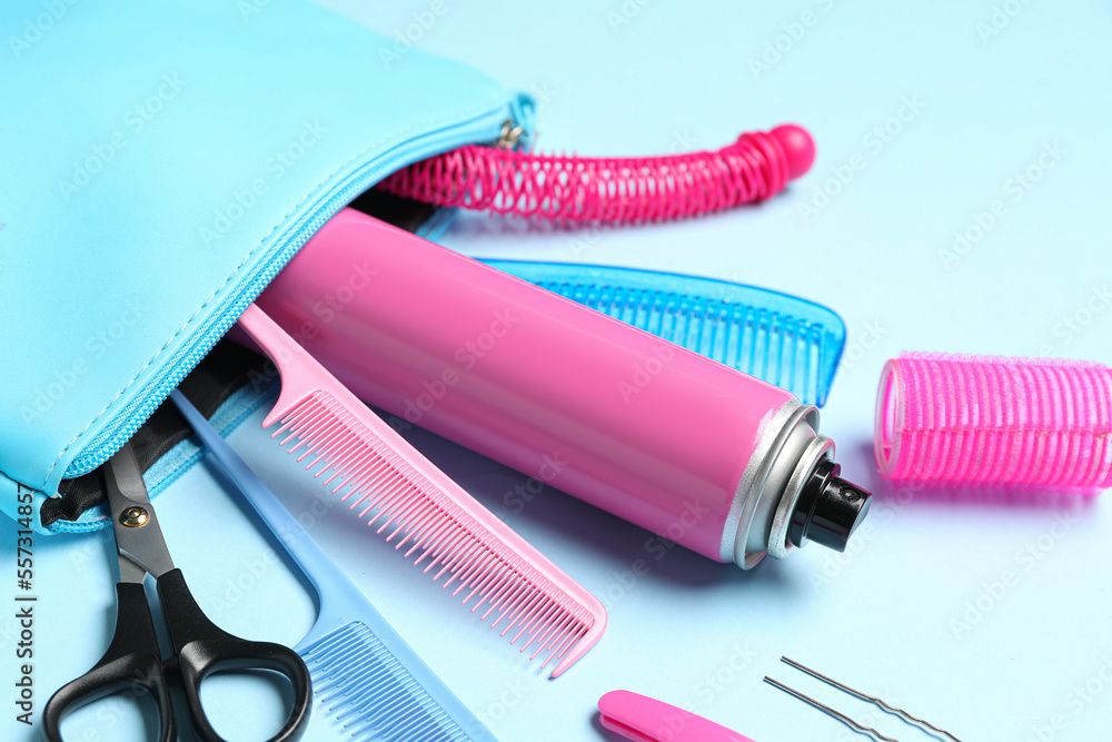 Bag with hair spray, combs, clips and scissors on blue background, closeup