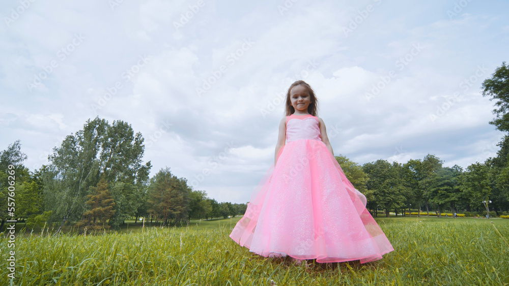 A girl in a pink princess dress is spinning in the park.