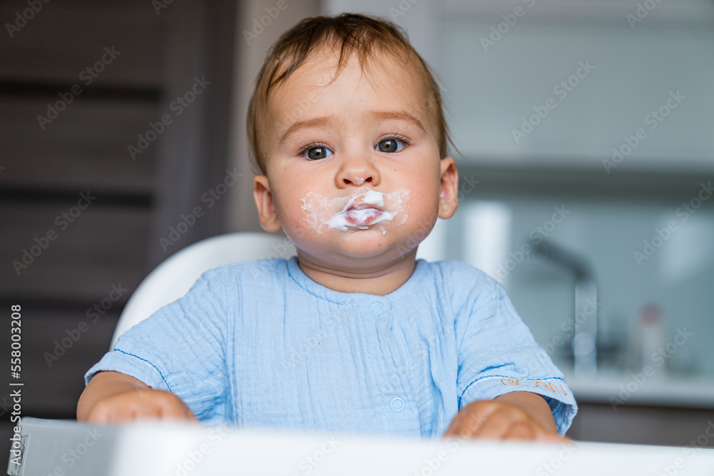 婴儿在厨房里吃东西。给婴儿喂婴儿食物。冷酷有趣的孩子在椅子上吃粥
