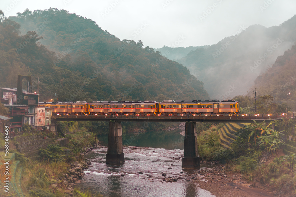 Trains pass over the bridge. The station next to a stream in a foggy valley. Sandiaoling Railway Sta