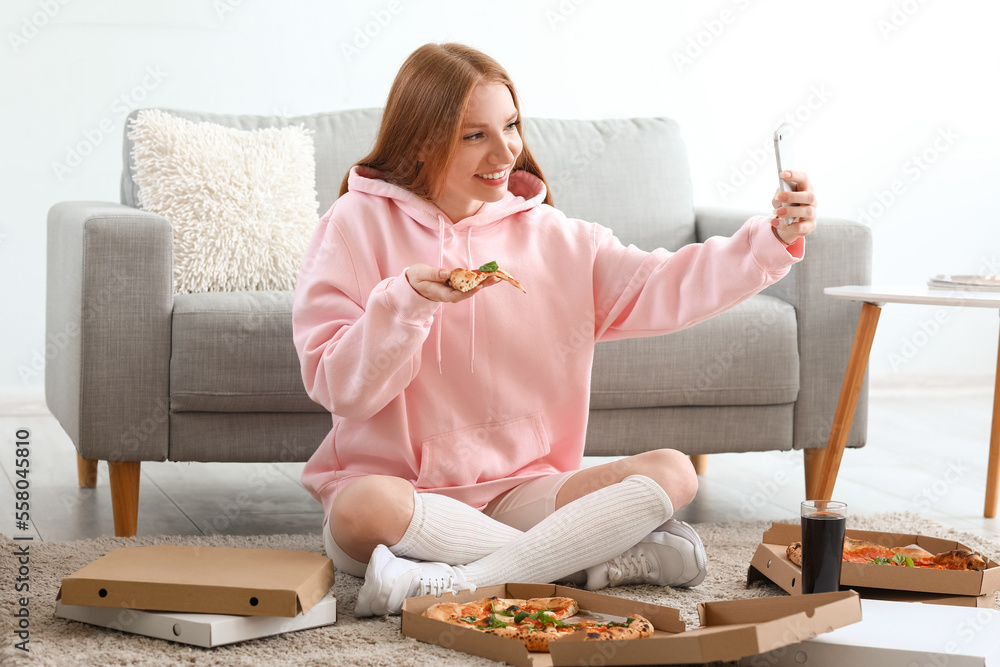 Young woman with tasty pizza taking selfie at home
