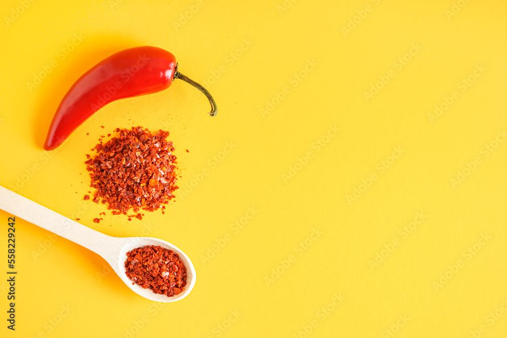 Spoon of chipotle chili flakes and fresh jalapeno pepper on color background