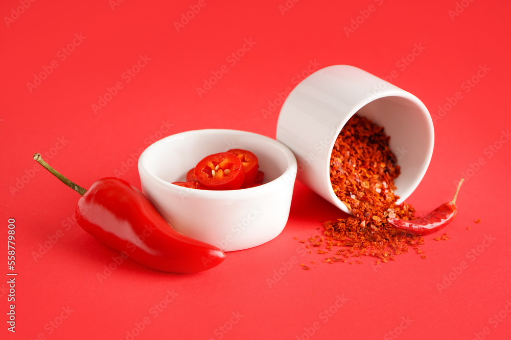 Bowls of chipotle chili flakes and fresh jalapeno pepper on red background