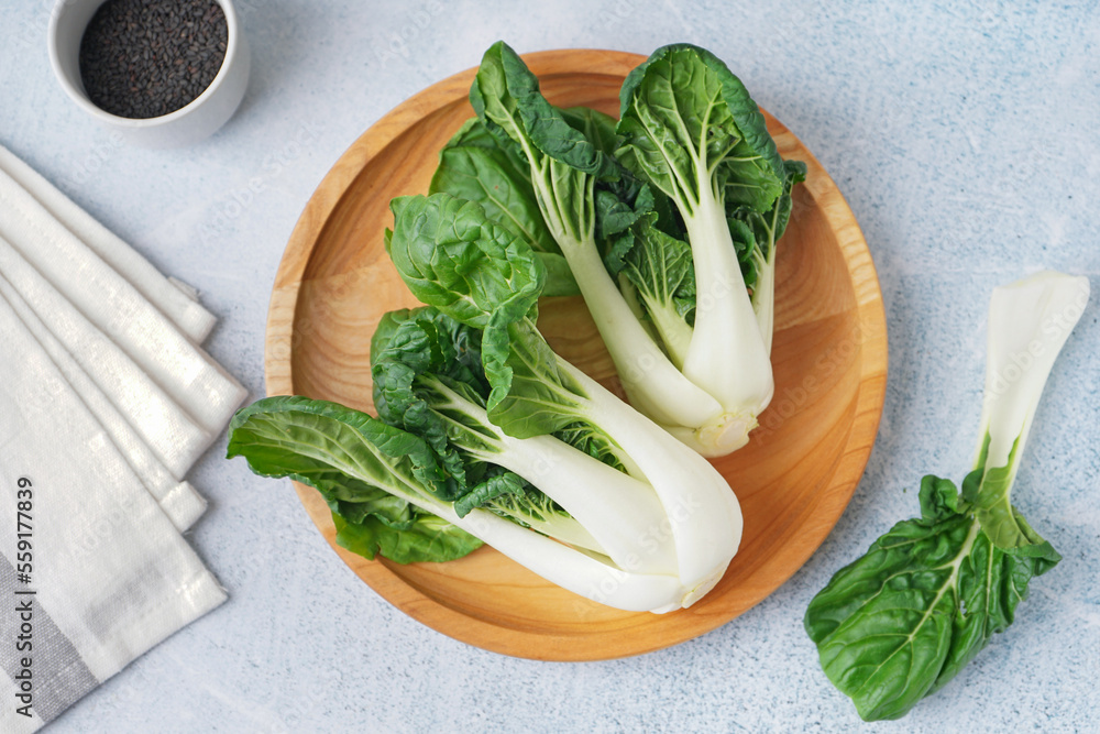 Wooden plate with fresh pak choi cabbage on light background